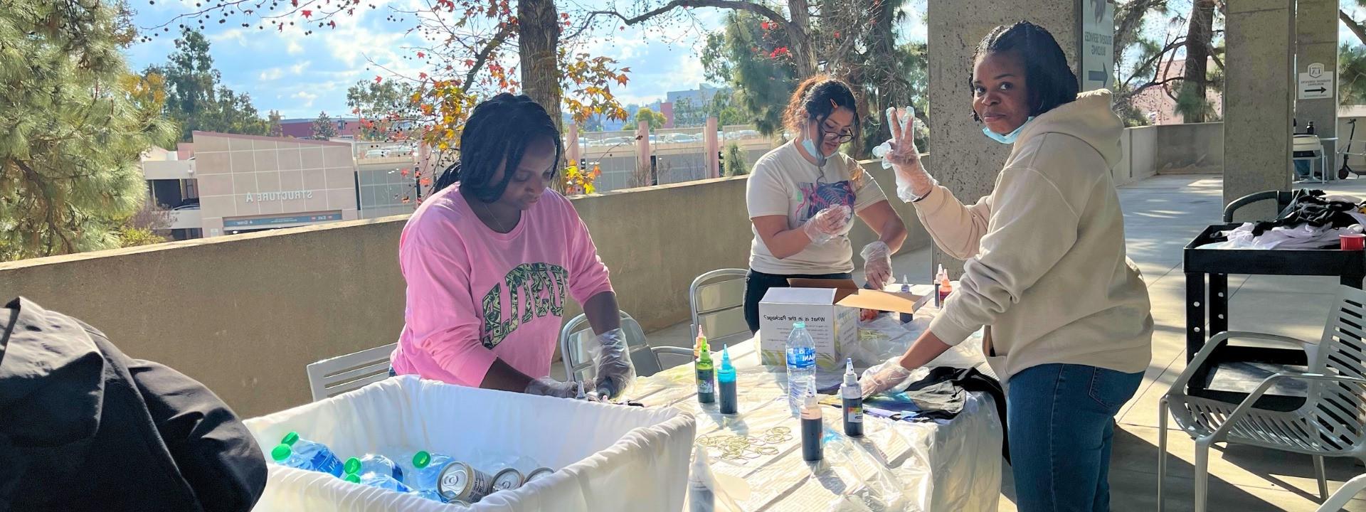 Three students smiling and creating a tie-dye shirt.